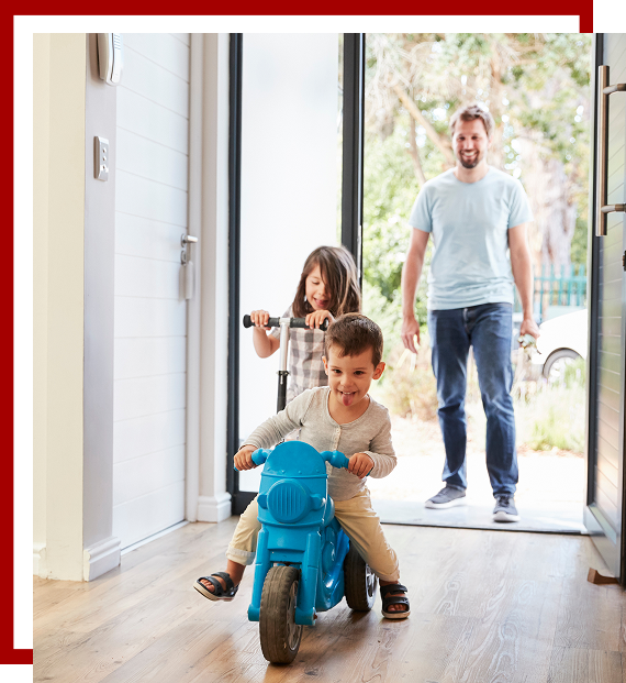 father and 2 children playing on scooter and bike in doorway of their home smiling