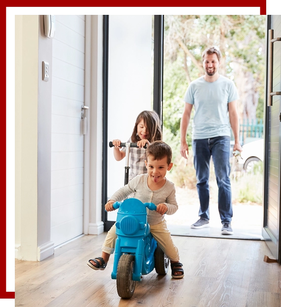 father and 2 children playing on scooter and bike in doorway of their home smiling